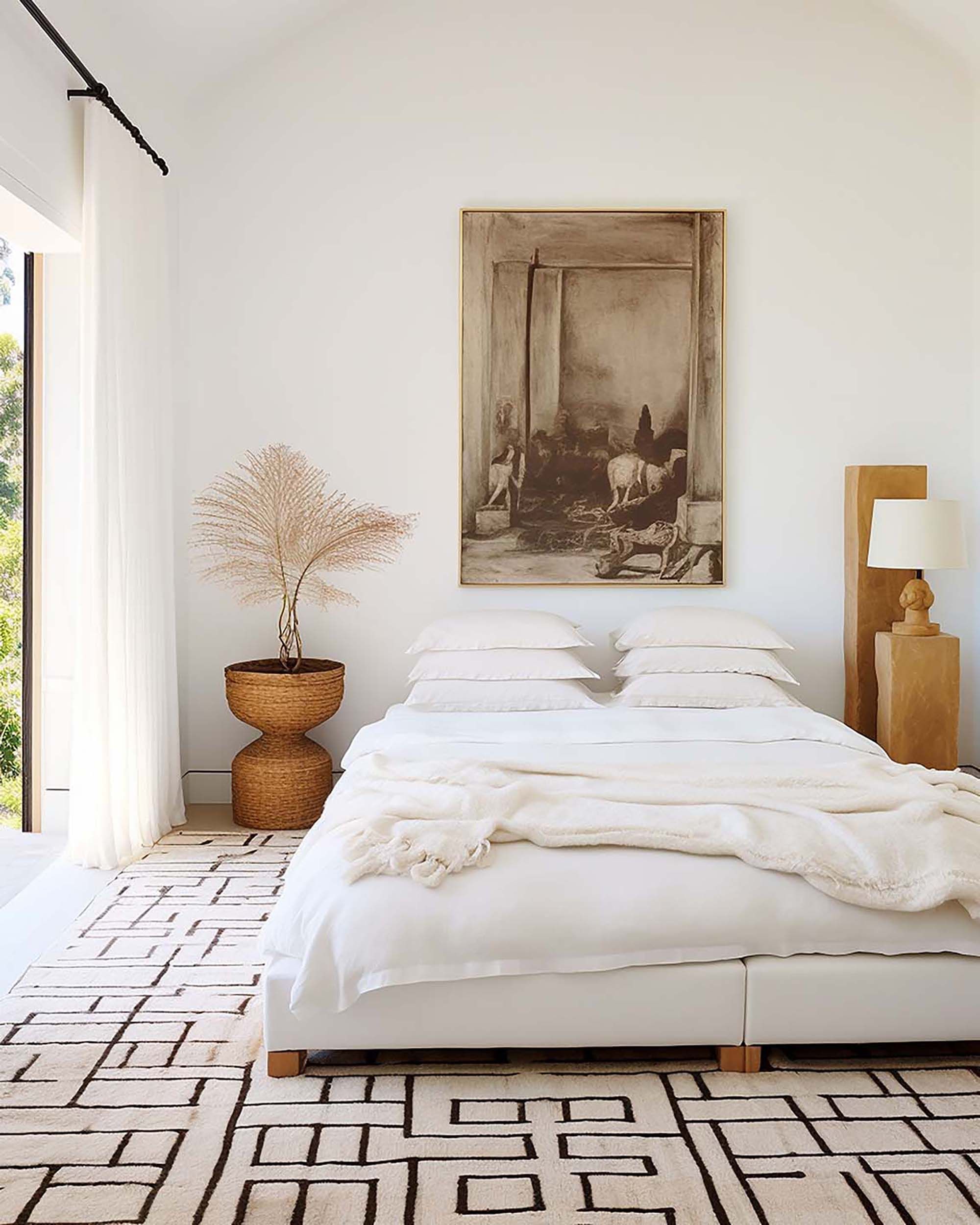 Bright minimalist bedroom with a customizable frame centered above a white bed, next to a woven side table and floor lamp.