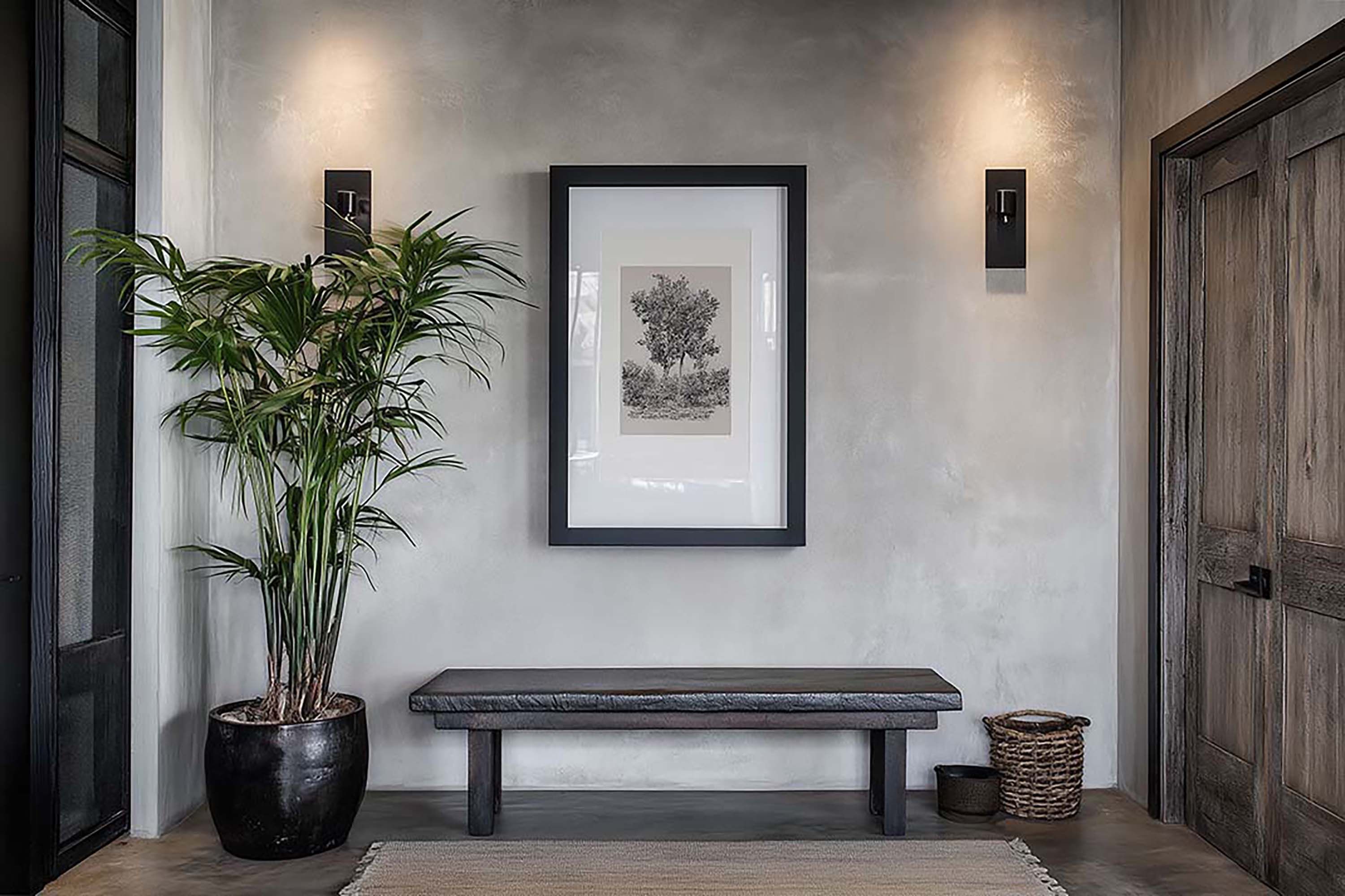 Modern rustic entryway wall with a black framed print above a low wooden bench, next to a tall potted plant.